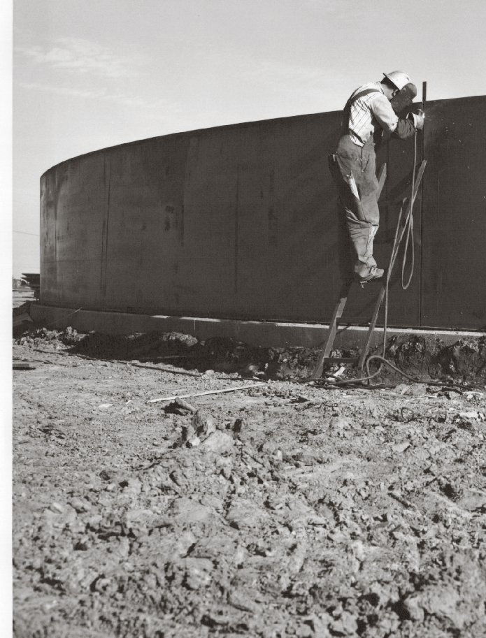 Black and white photo of a worker on a ladder inspecting a concrete reservoir under construction