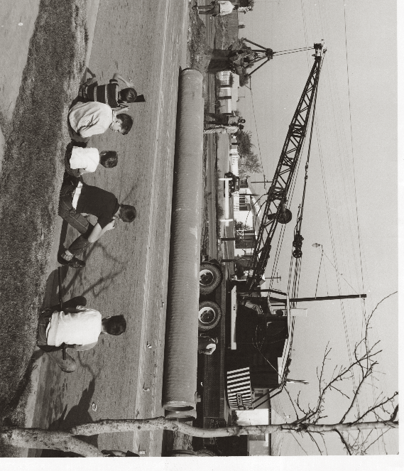 Historical black-and-white photograph of pipeline construction with children watching a crane